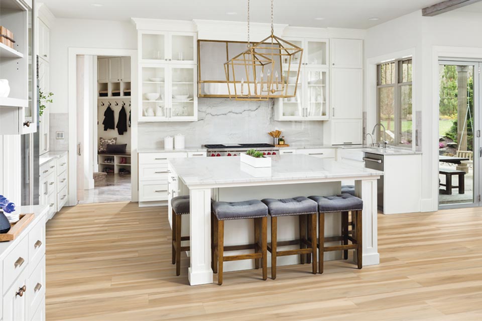 warm toned luxury vinyl flooring in kitchen with white cabinets and kitchen island with wood stools and mixed metal decor.